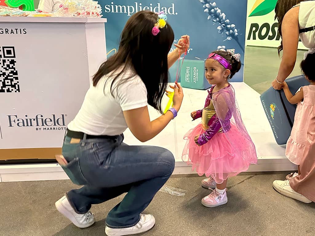 edecan entregando articulos promocionales personalizados a una niña en el stand publicitario de Fairfield en una expo CDMX